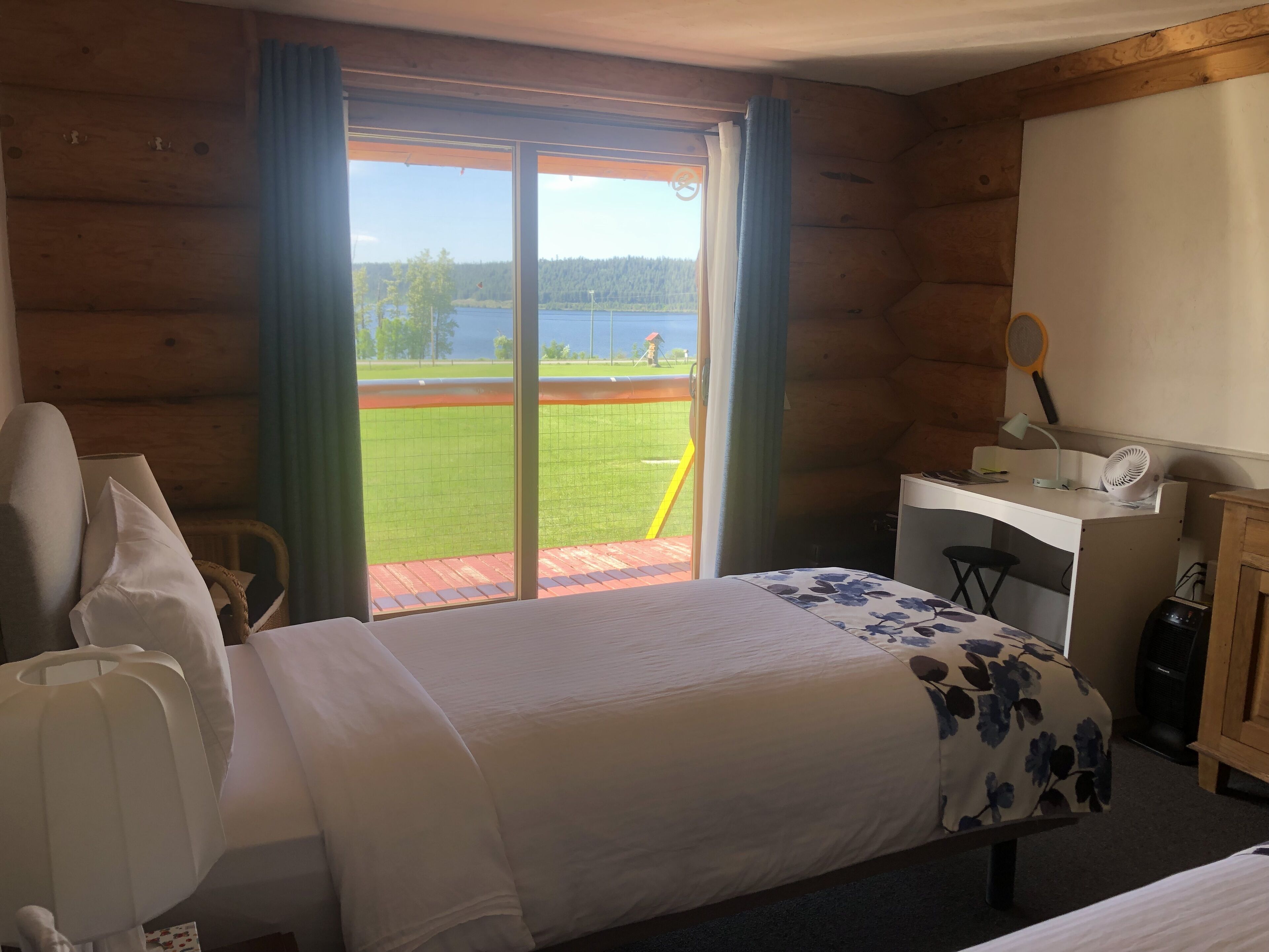 Une chambre dans un chalet en bois, avec un lit, un bureau et une vue sur un champ verdoyant et un lac.