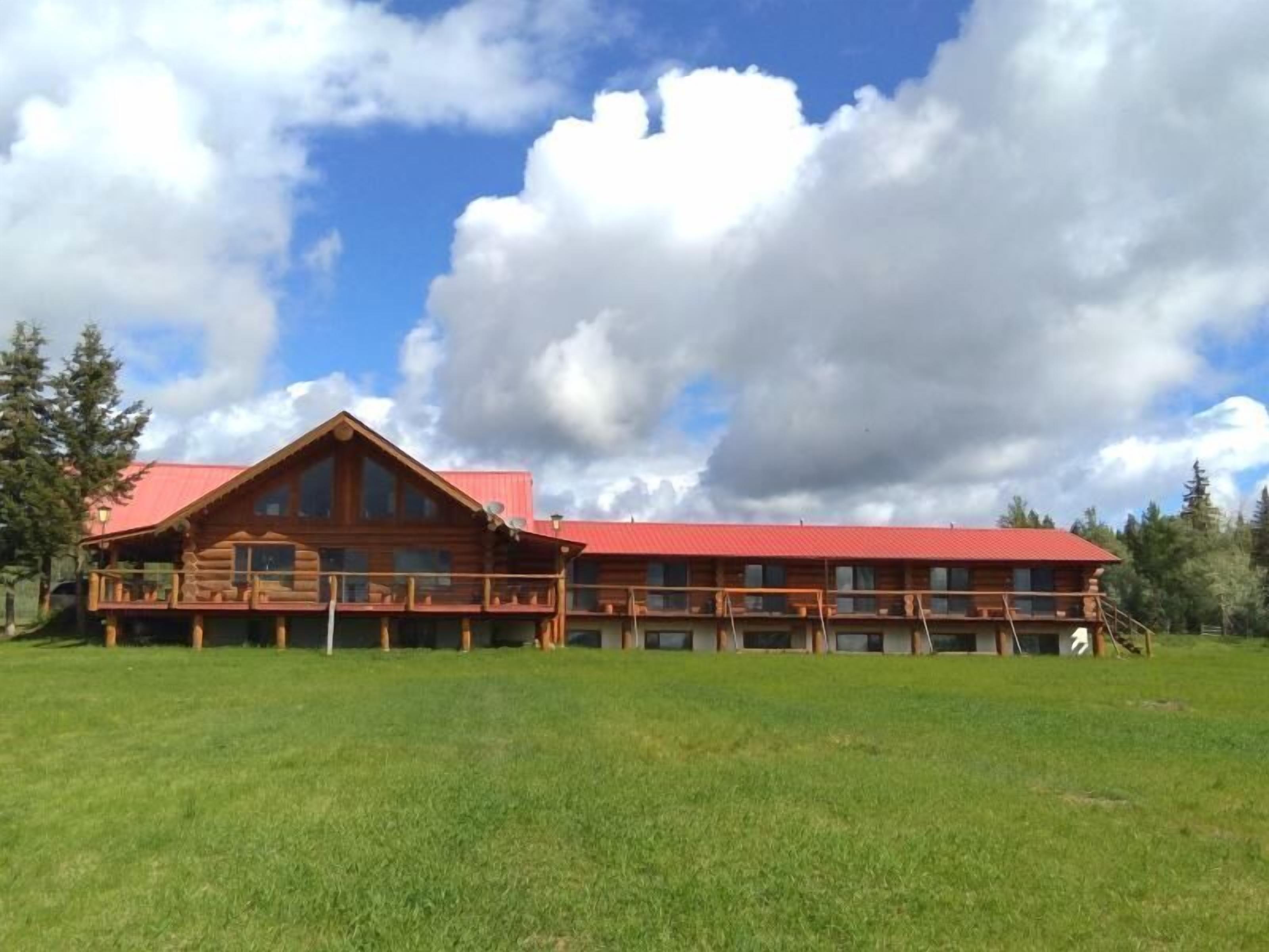 Un amplio refugio de madera con techo rojo, varios balcones y un espacioso patio cubierto de césped.