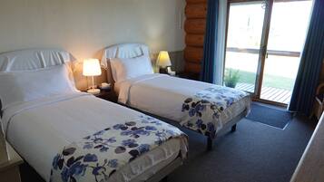 Camera d'albergo con due letti, ciascuno con una coperta a fiori, lampade sui comodini e vista sull'esterno tramite una porta scorrevole in vetro.