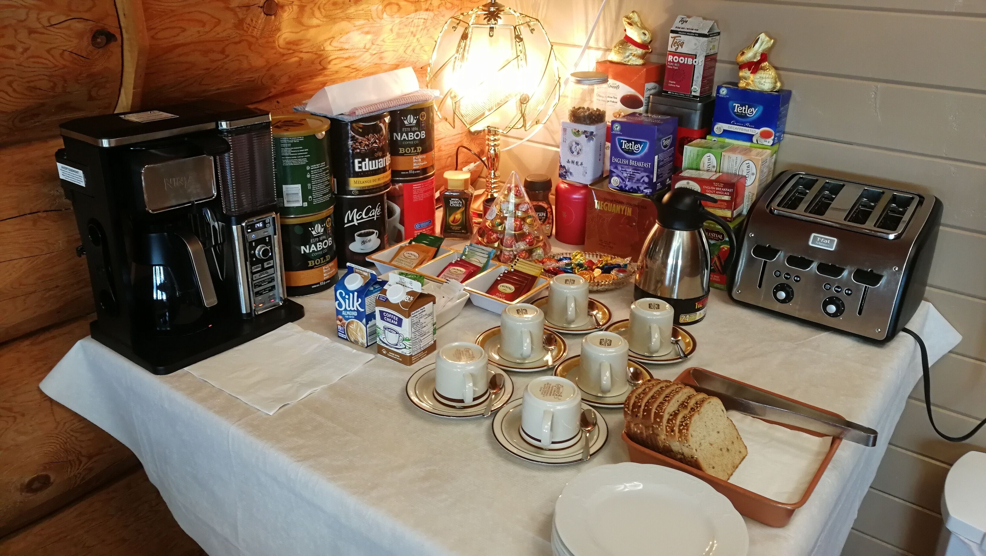A breakfast setup with coffee makers, tea, and pastries on a table.