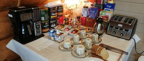 Une table dressée pour le petit-déjeuner, avec des machines à café, du thé et des viennoiseries.