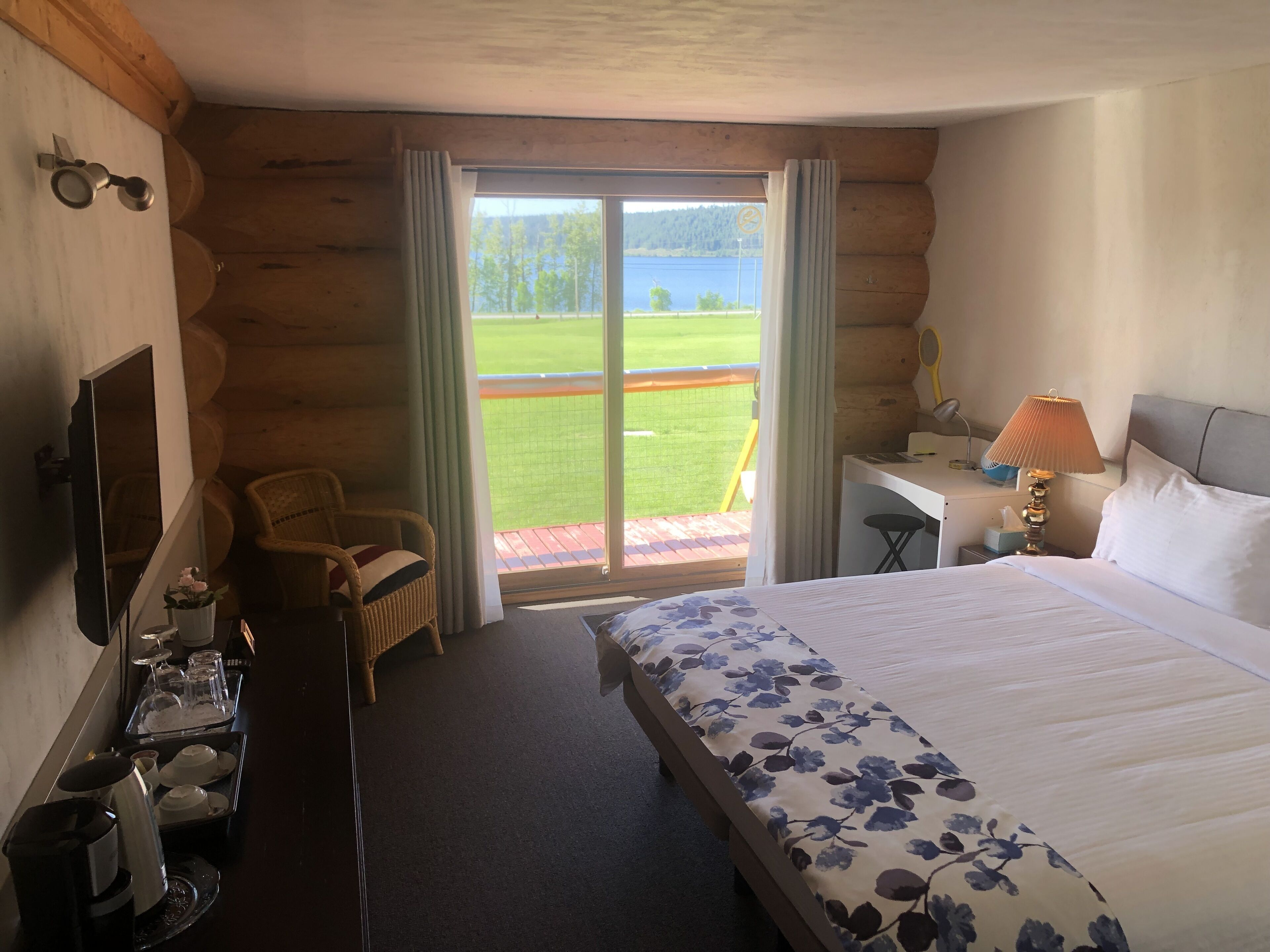 Ein Hotelzimmer mit Bett, Schreibtisch, Stuhl, Fernseher und Blick auf eine grüne Landschaft durch ein großes Fenster.