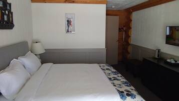 A hotel room with a bed, a bedside table with a lamp, a painting on the wall, and a television on the opposite wall.