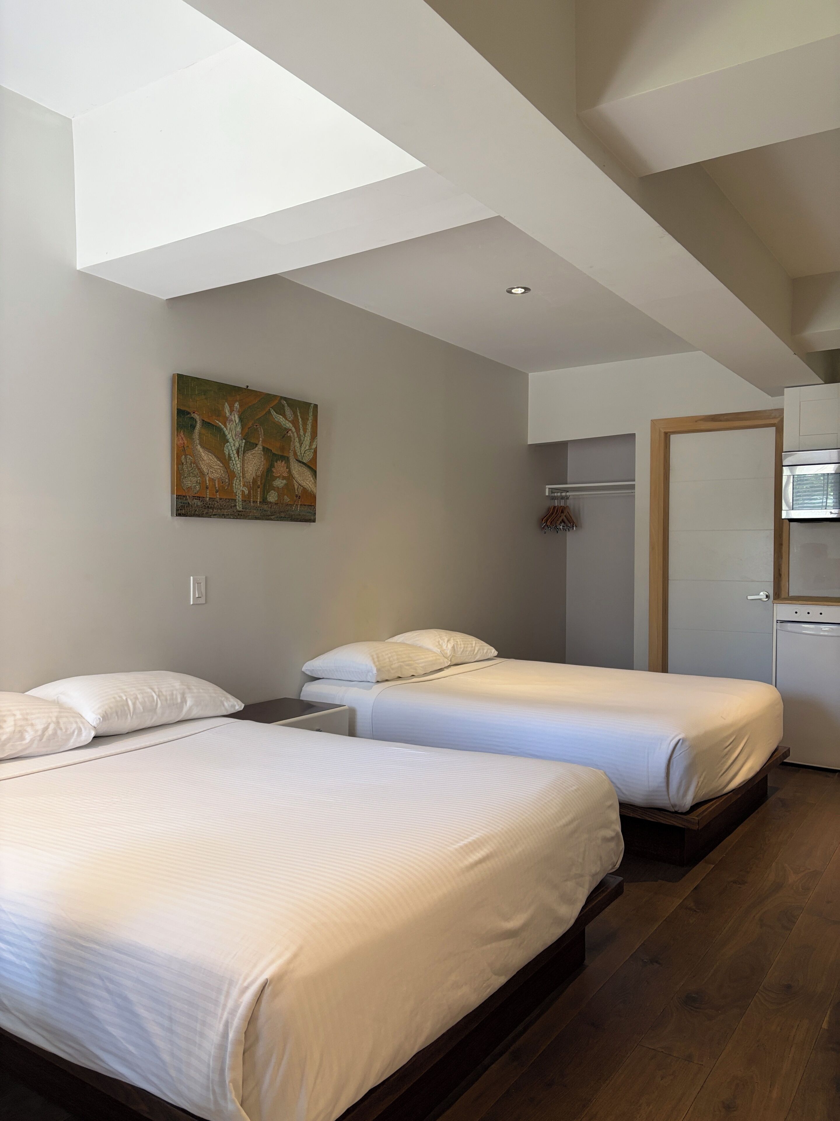 A hotel room with two beds, a painting on the wall, a microwave, and a door.
