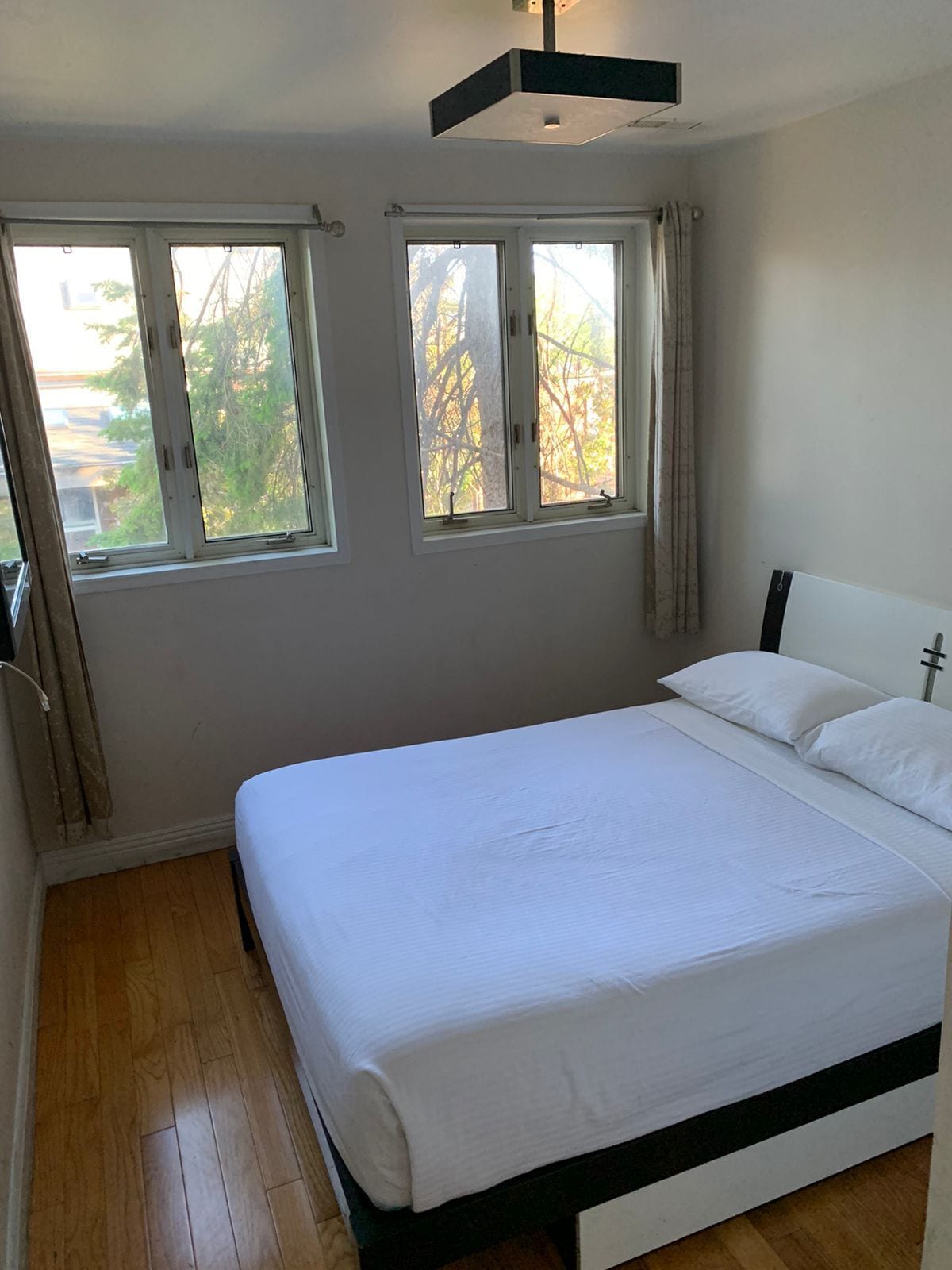 A bedroom with a bed, two windows, and a ceiling light fixture.