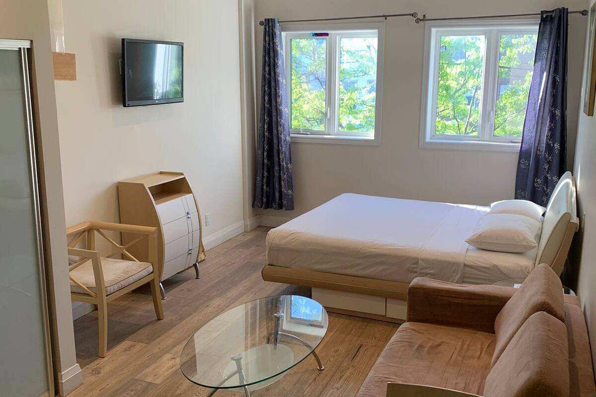 Ett modernt hotellrum med en säng, en soffa, ett soffbord i glas, en tv och ett fönster med gardiner.