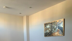 A hotel room with two single beds, a small bedside table, a wall-mounted artwork, and a tiled floor.