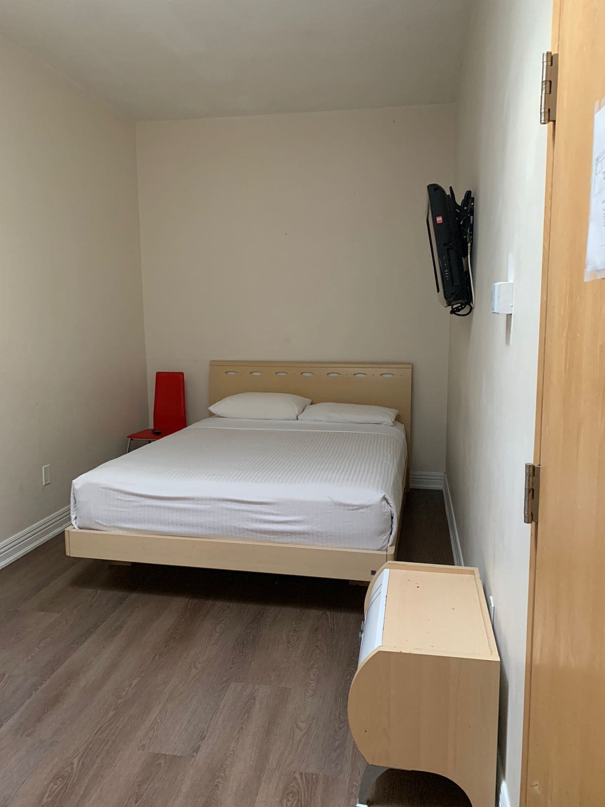 A small, single-bed room with a wooden headboard, a red chair, and a wooden desk.