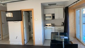 A compact kitchen with white cabinets, a microwave, and a dishwasher. There is a glass table with chairs and a TV mounted on the wall.
