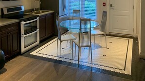 A compact kitchen with dark cabinets, a microwave, and an oven. There's a glass dining table with four chairs and a window with blinds.