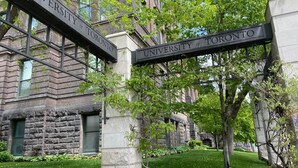 A stone building with a sign reading "University of Toronto" and a well-maintained lawn.