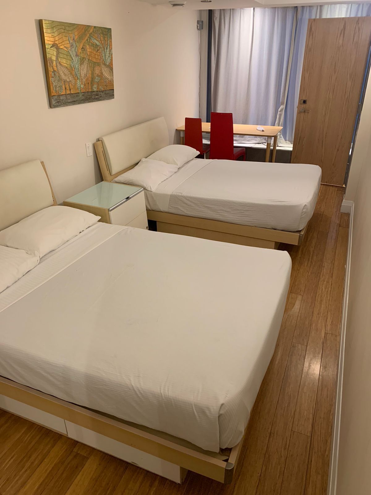Una habitación de hotel con dos camas, una mesita, una silla y un cuadro en la pared.