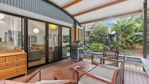 An outdoor deck with a grill, wooden furniture, and a view of a tropical garden.