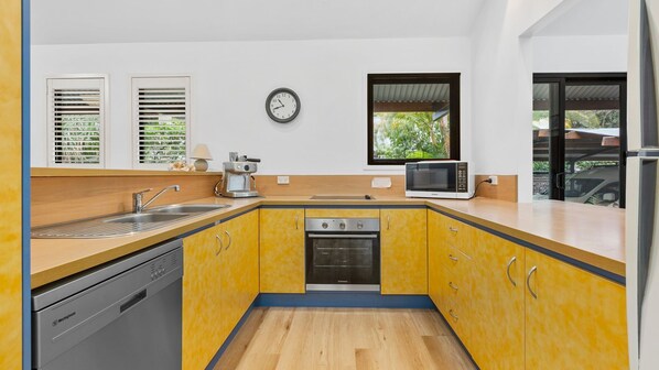A compact kitchen with yellow cabinets, a built-in oven, a microwave, and a coffee maker. - 43 Satinwood Drive - Rainbow Shores. Pet Friendly and Air Conditioned! (Rainbow Beach)