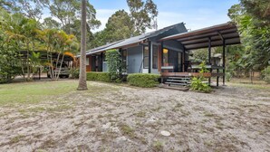 A modern house with a covered patio, surrounded by lush greenery and a sandy yard.