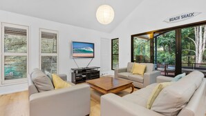 A modern living room with a television, two sofas, a coffee table, and large windows offering a view of the outdoors.