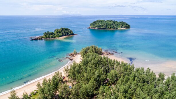 Un paisaje costero con dos islas pequeñas, aguas turquesas transparentes y una playa con un bosque denso al frente.