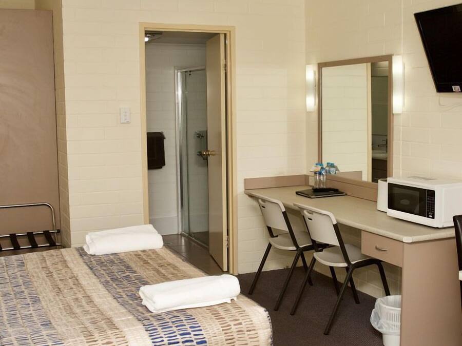 A hotel room with a bed, a desk with a chair, a microwave, a TV, and a bathroom door.