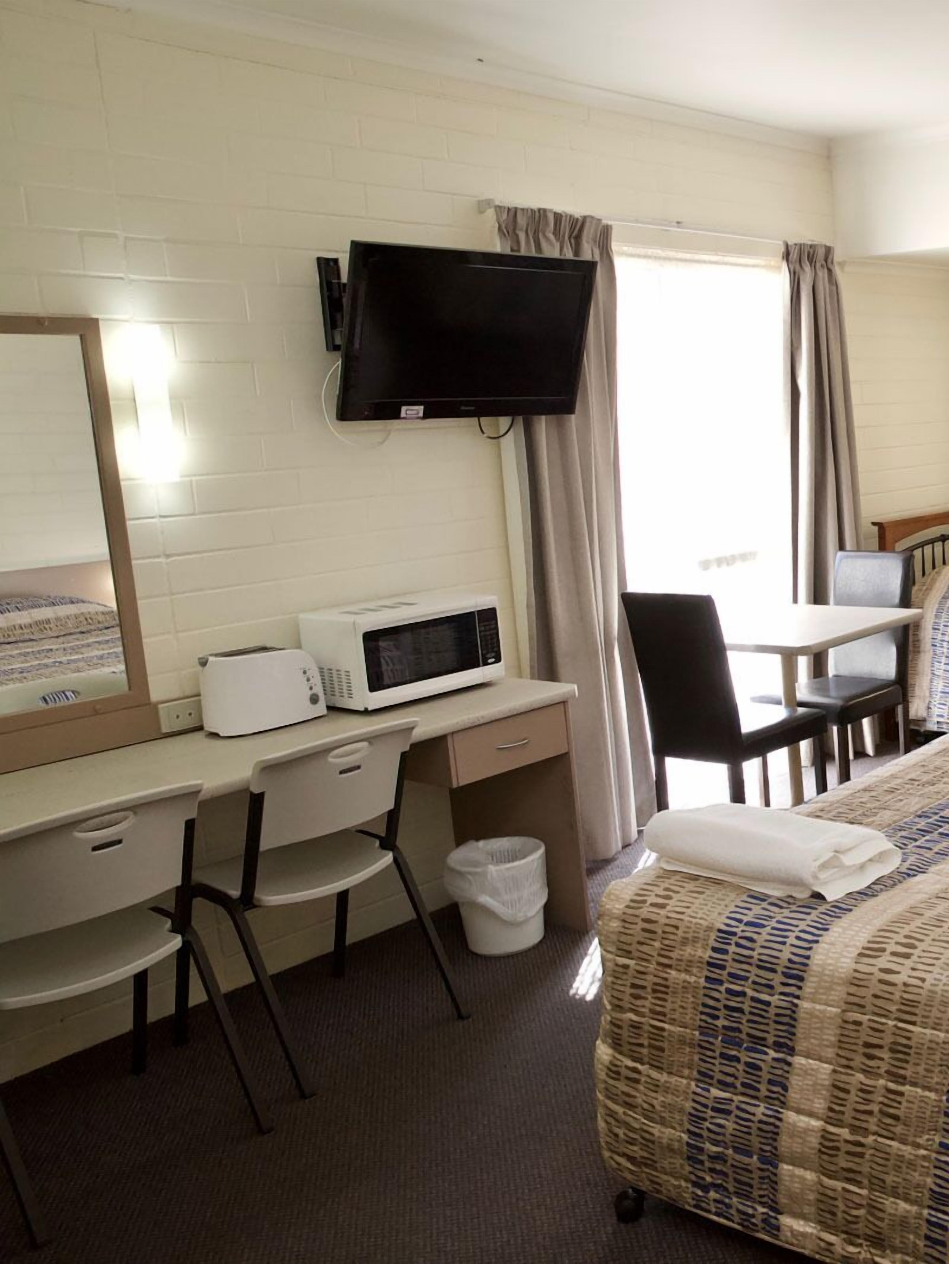 Habitación de hotel con cama, escritorio con microondas, televisión montada en la pared y ventana con cortinas.