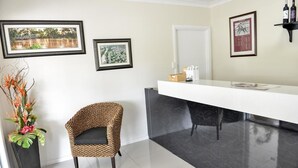 A modern bathroom with a black marble vanity, framed artwork on the walls, and a wicker chair. - Pioneer Motel (Goondiwindi)