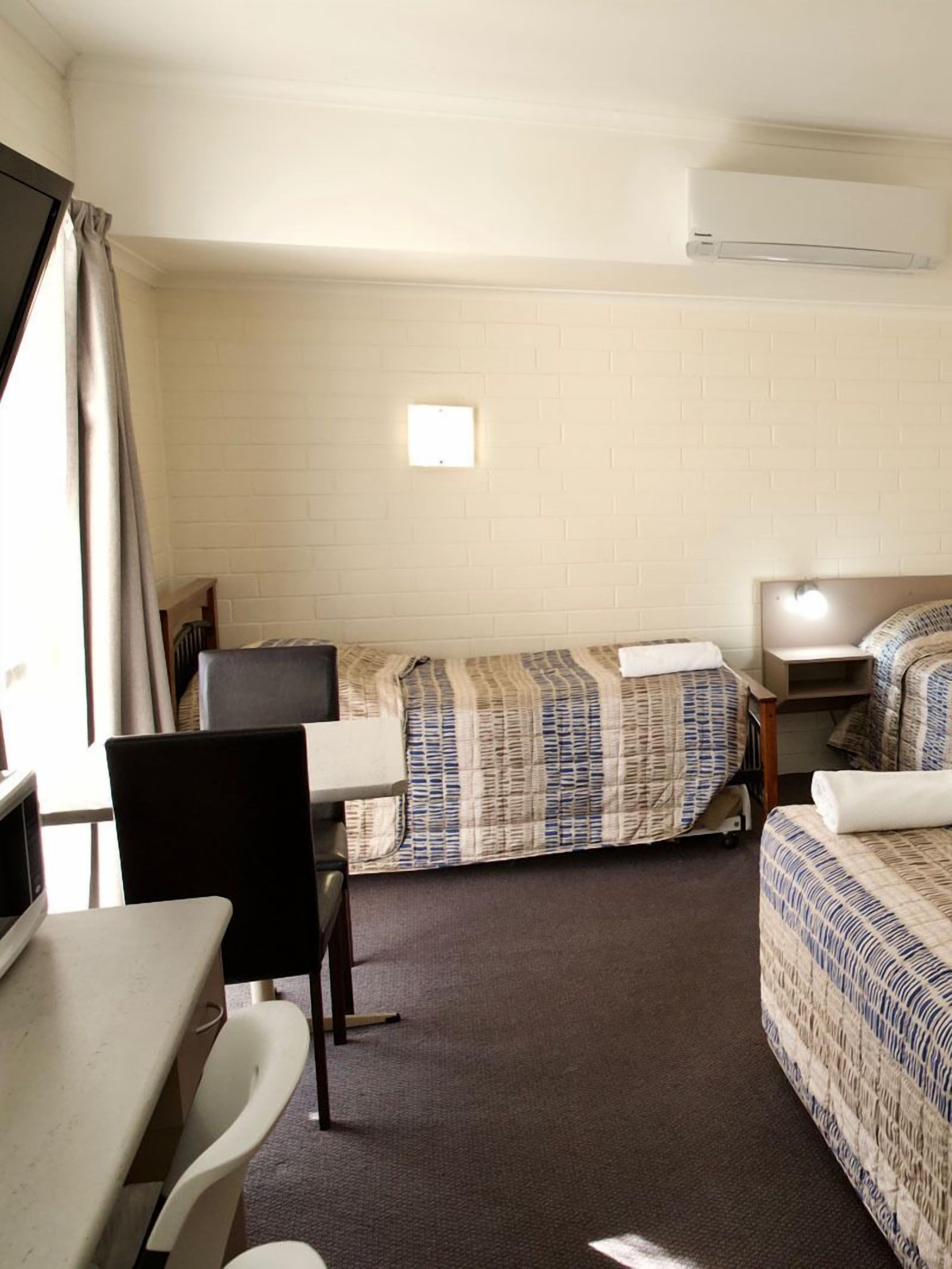 Habitación de hotel compacta con dos camas, un escritorio, una silla y un televisor.