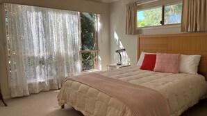 Een slaapkamer met een groot bed, een nachtkastje, een lamp en een raam met gordijnen.