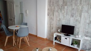 A living room with a TV on a white stand, a dining table with chairs, and a small white cabinet with decorative items. - Fantastic apartment (El Morche)