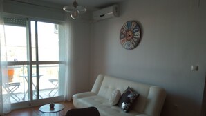A living room with a white sofa, a coffee table, a wall clock, and a view through a glass door to an outdoor patio. - Fantastic apartment (El Morche)