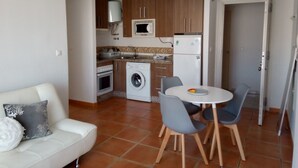 A compact kitchen with a washing machine, microwave, and refrigerator. There is a dining table with chairs and a white sofa with a decorative pillow. - Fantastic apartment (El Morche)