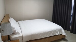 Uma cama bem arrumada com roupa de cama branca, uma cabeceira de madeira e uma luminária cinza em uma mesa de cabeceira.