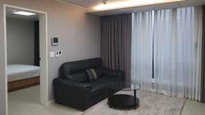 Quarto de hotel moderno com um sofá de couro preto, uma mesa de centro de vidro e uma cama no quarto adjacente.