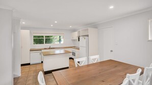 A modern kitchen with white cabinetry, a wooden dining table, and white chairs. - COOLAMAINE 1 - Rainbow Beach. Easy walk to beach and shops. (RAINBOW BEACH)