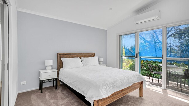 A bedroom with a large bed, a nightstand, a wall-mounted air conditioner, and a sliding glass door leading to an outdoor area. - COOLAMAINE 1 - Rainbow Beach. Easy walk to beach and shops. (RAINBOW BEACH)