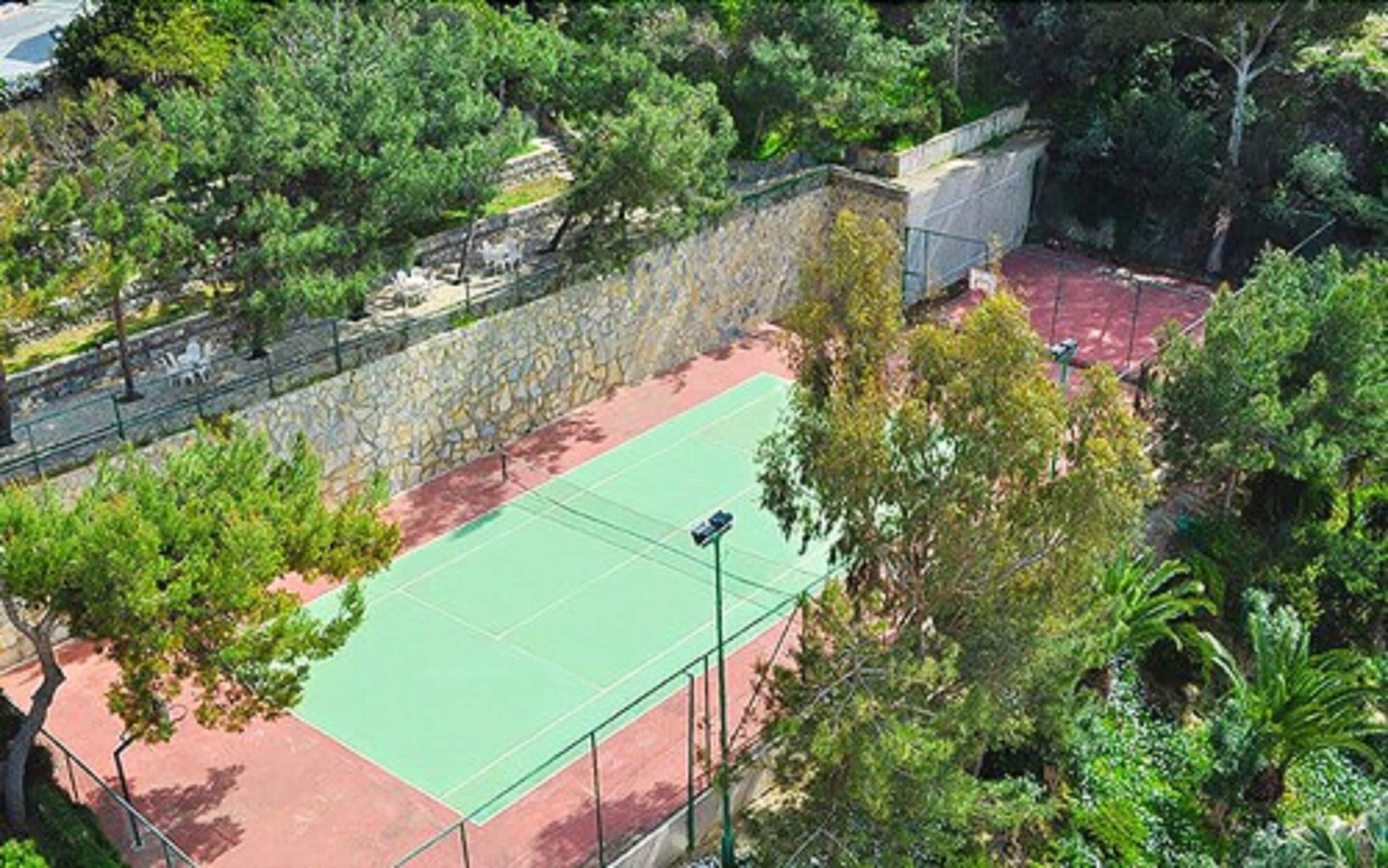 Una cancha de tenis al aire libre rodeada de árboles y un muro de piedra.