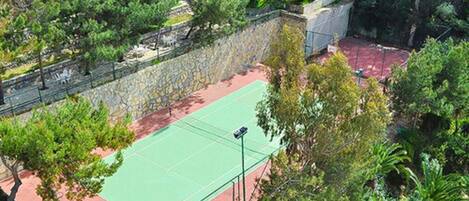 Una cancha de tenis al aire libre rodeada de árboles y un muro de piedra.
