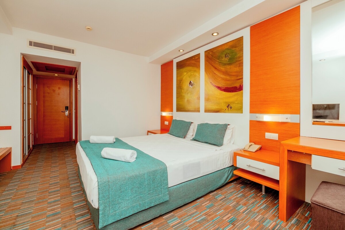 A hotel room with a bed, a desk, a chair, a phone, and a painting on the wall.