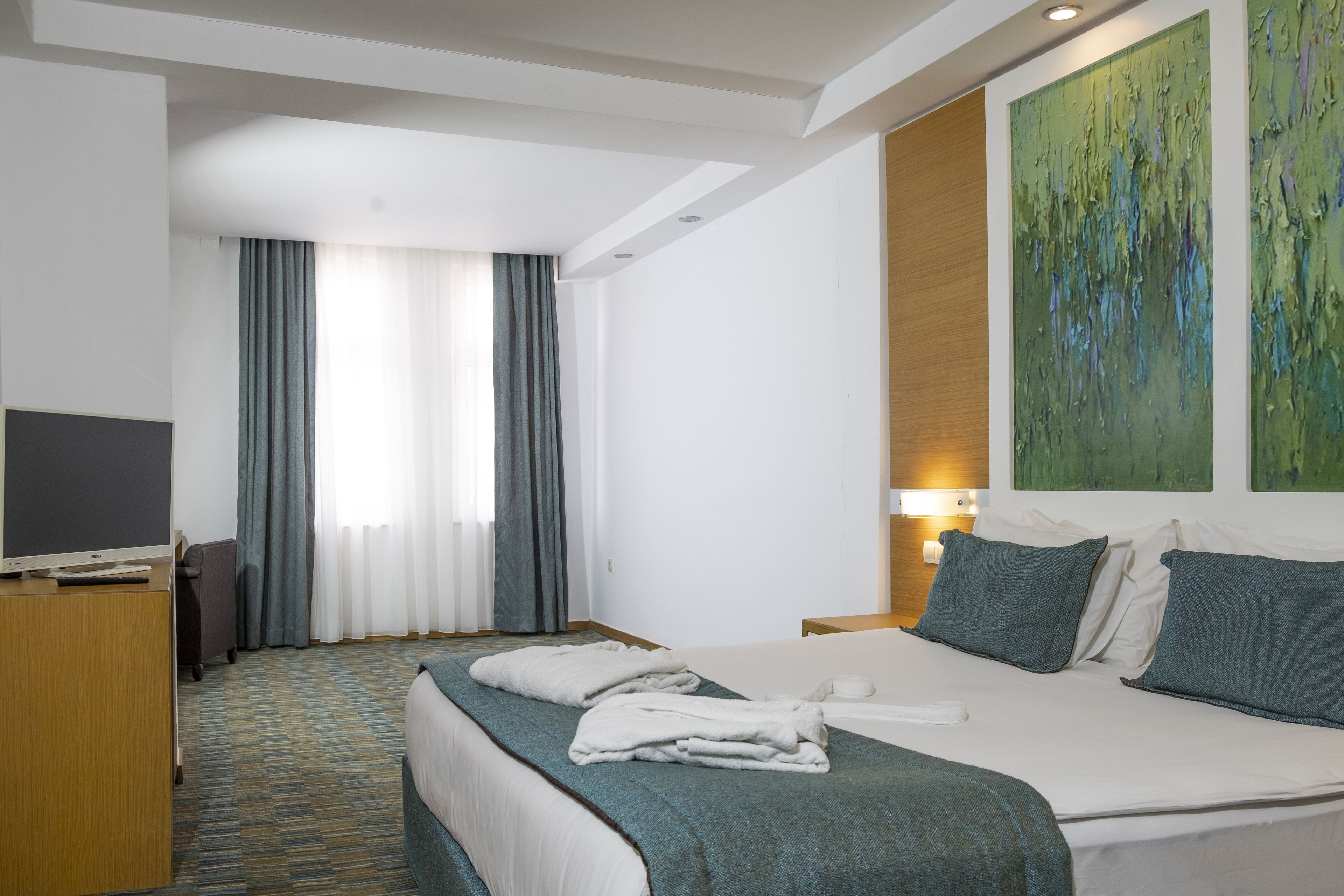 Une chambre d’hôtel avec un lit, un bureau équipé d’un ordinateur, une télévision et une fenêtre avec des rideaux.