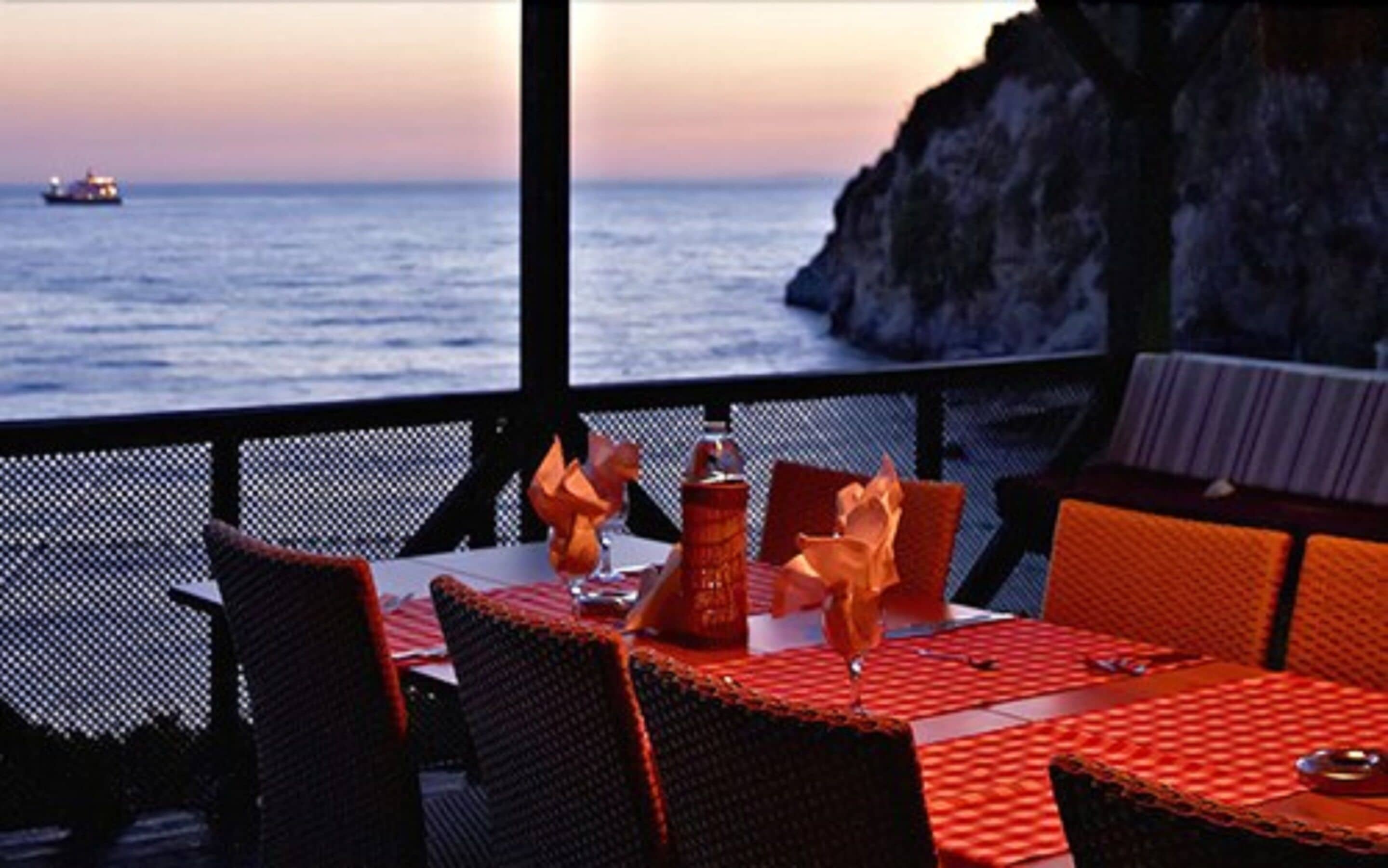 An outdoor dining area with a view of the sea and a rocky cliff.