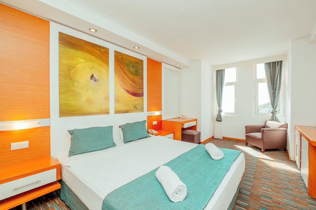 A hotel room with a bed, a desk, a chair, and a large window.