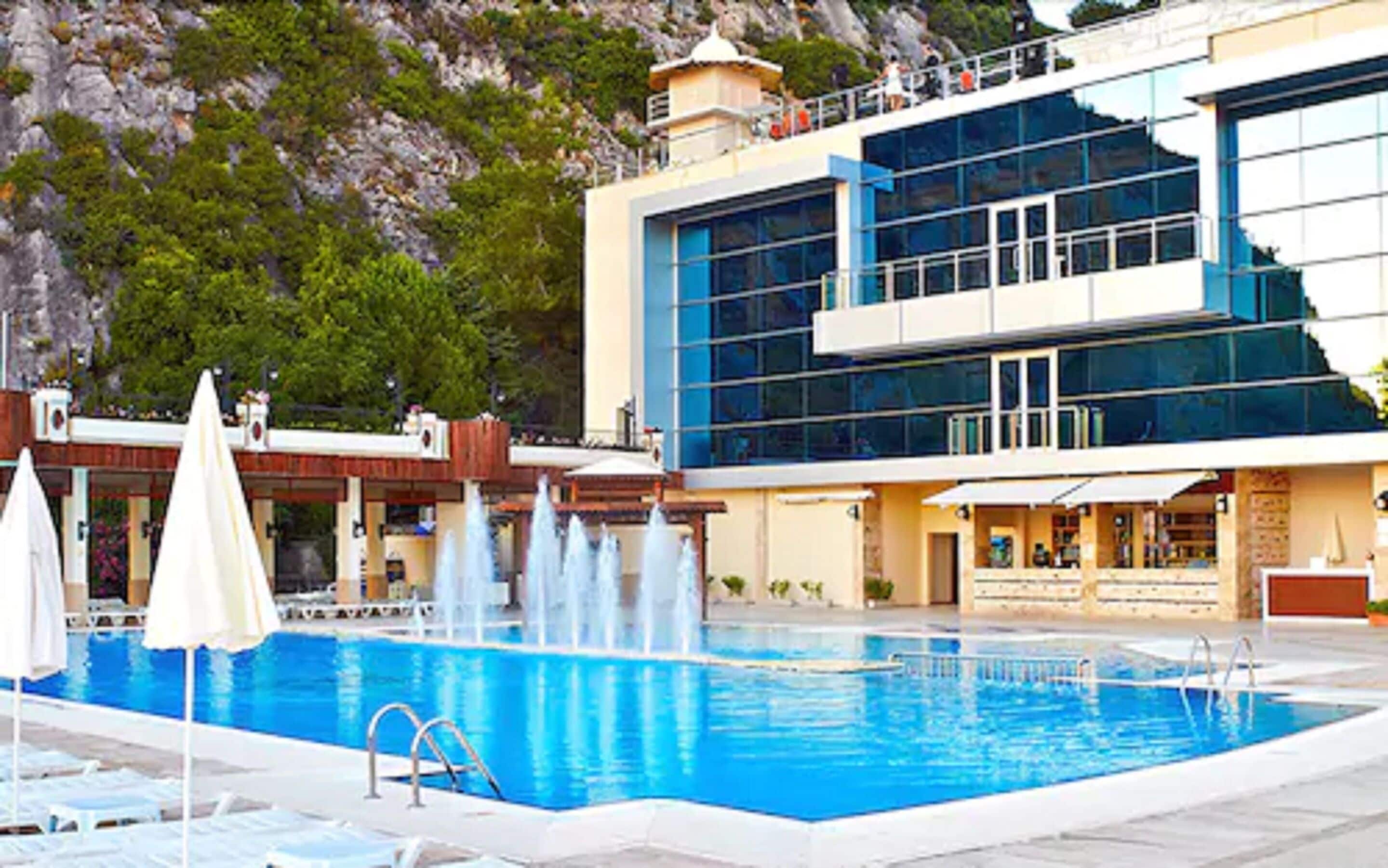 A swimming pool with a water fountain, surrounded by lounge chairs and umbrellas.