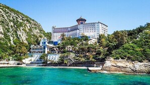 Un hotel costero con una torre destacada, rodeado de exuberante vegetación y aguas turquesas cristalinas.