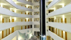 Interior de un hotel de varios niveles con balcones, una escalera central y un mural de un águila.