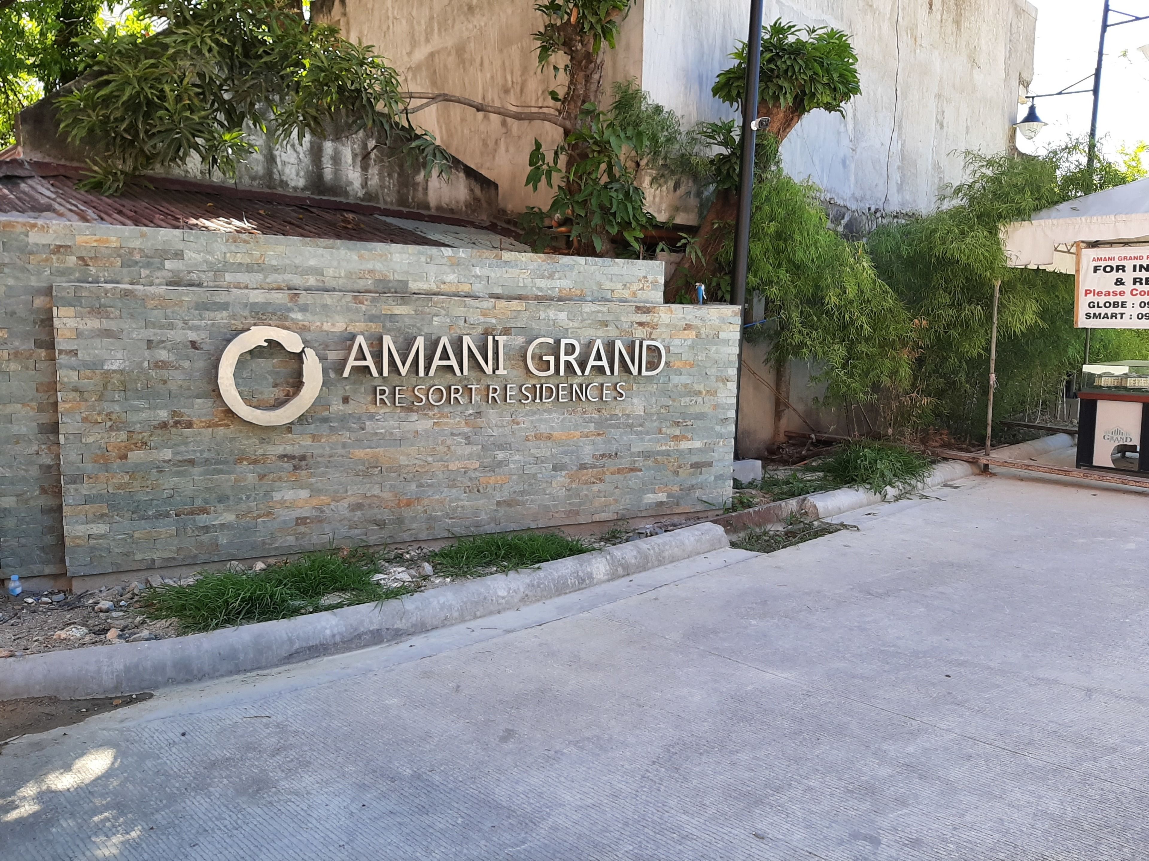 Ένας τοίχος από πέτρα με την επιγραφή «AMANI GRAND RESORT RESIDENCES» και ένα κυκλικό λογότυπο.