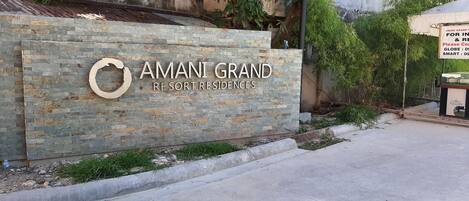 Ένας τοίχος από πέτρα με την επιγραφή «AMANI GRAND RESORT RESIDENCES» και ένα κυκλικό λογότυπο.