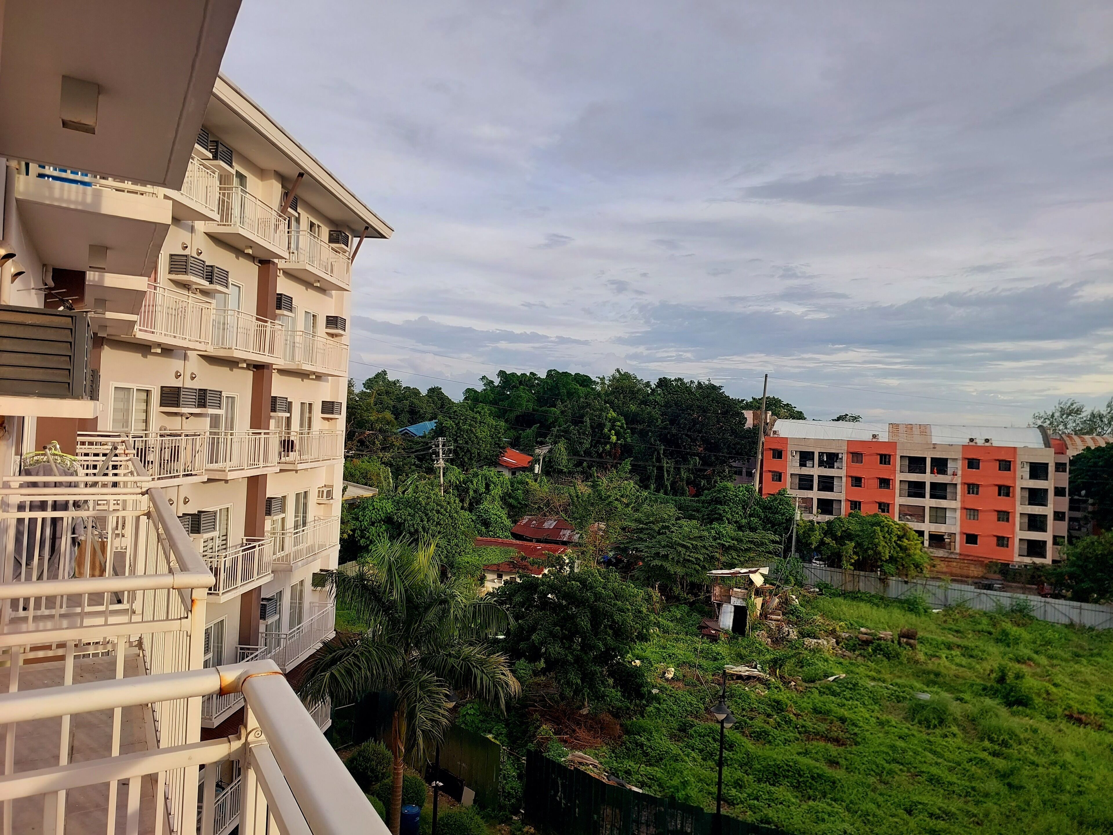 A multi-story residential building with balconies, surrounded by greenery and other buildings.