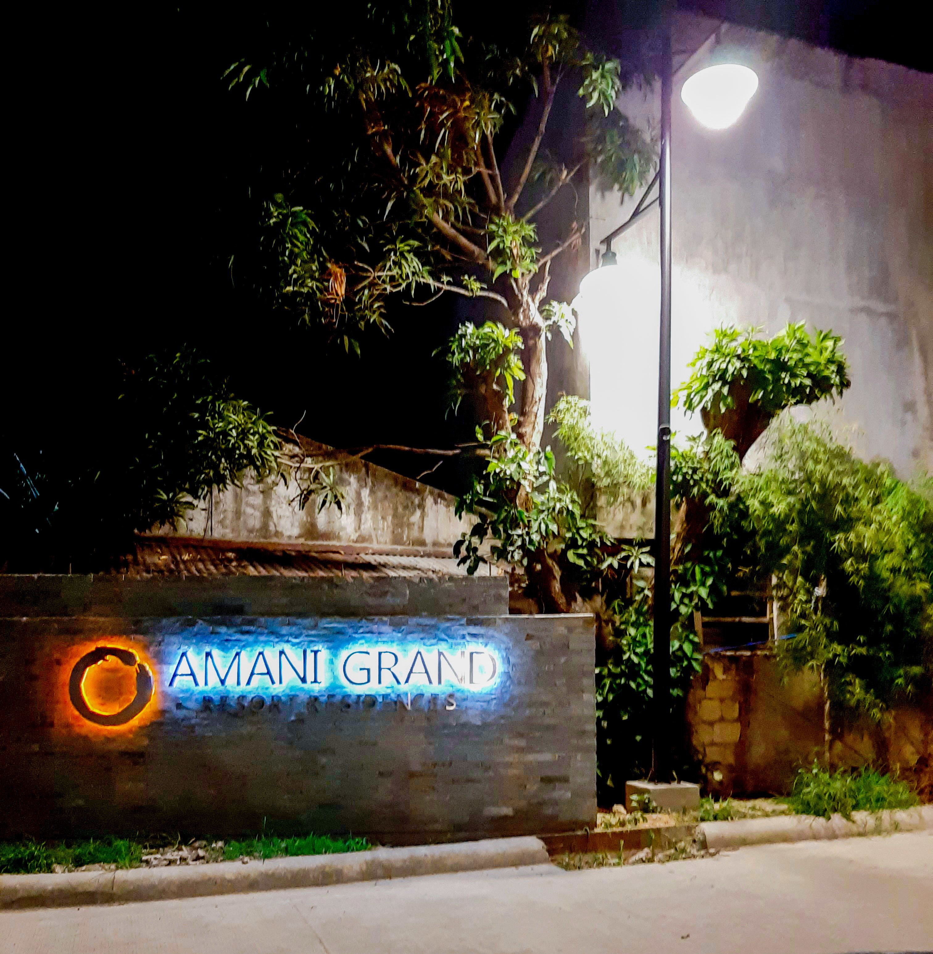 A nighttime view of a building entrance with a sign reading "AMANI GRAND SHOPPING CENTER".