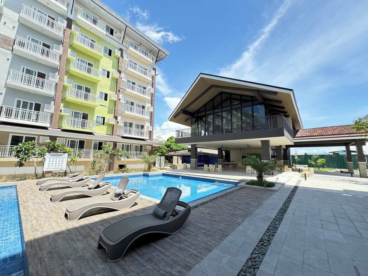 Un hotel moderno con piscina, sillas de descanso y un espacio exterior techado.