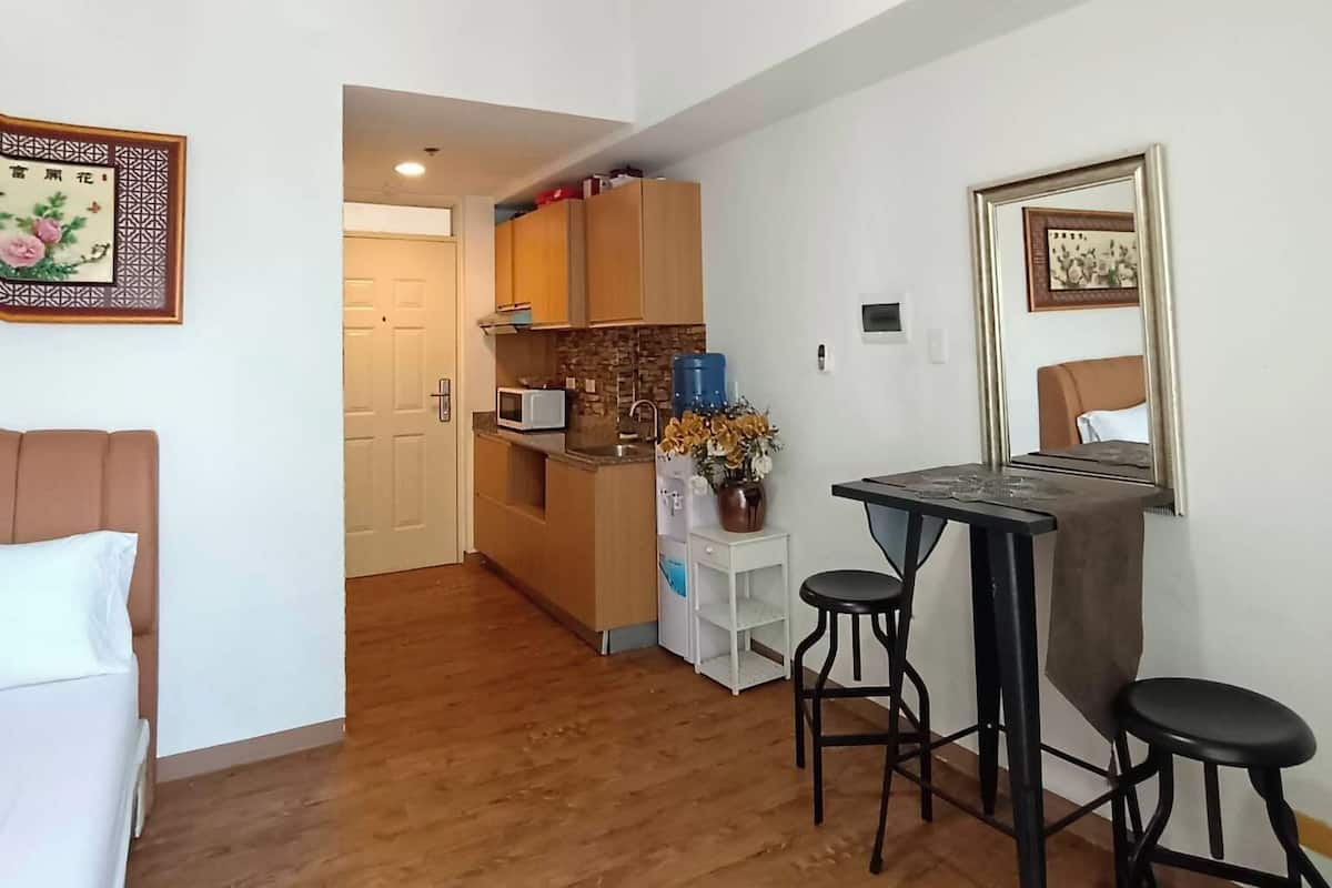 Um espaço compacto com cozinha compacta, área de jantar com mesa e dois banquinhos, cama e luminária de teto.