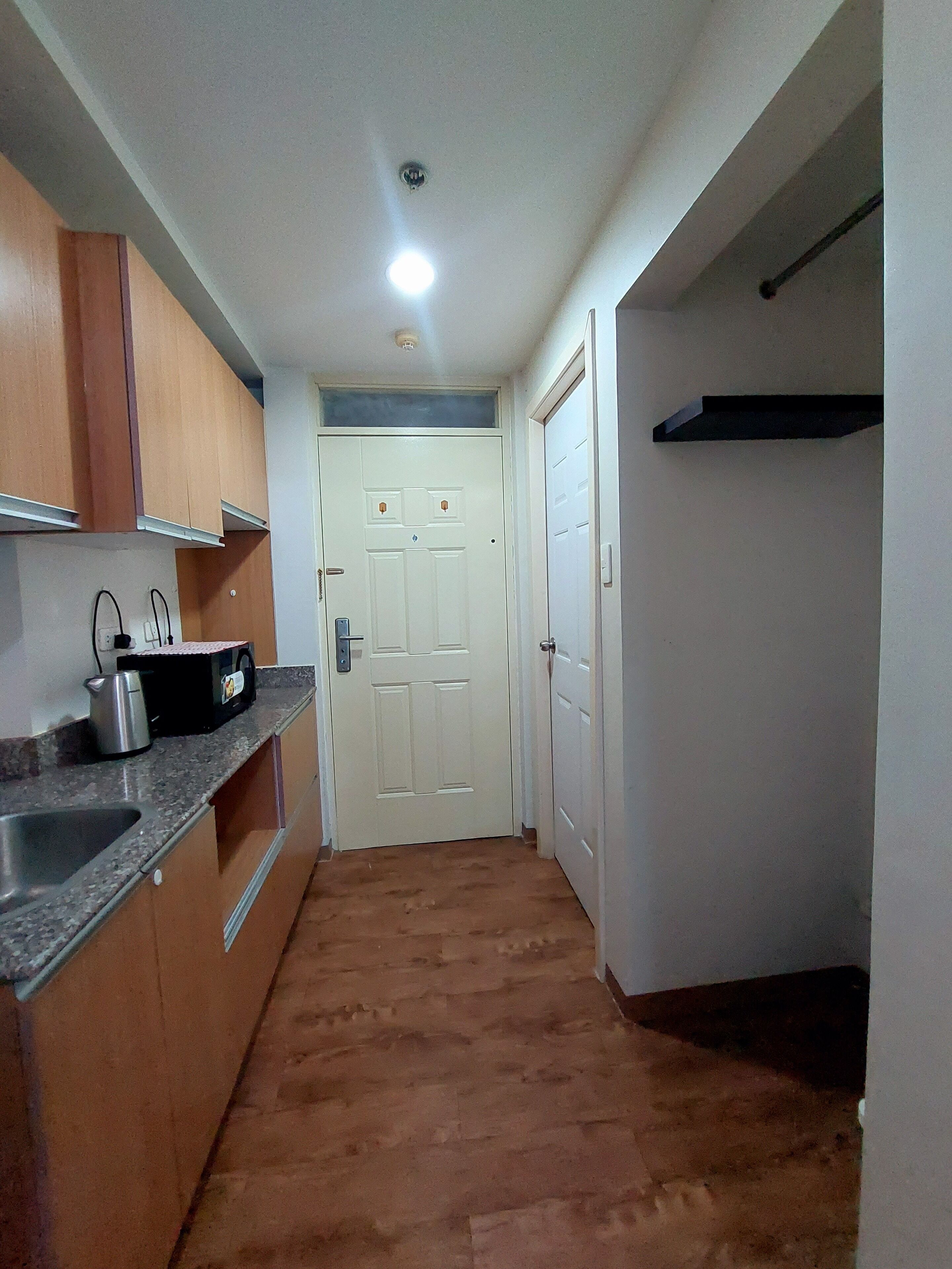 Un pasillo estrecho con una zona de cocina a un lado, que incluye armarios, un lavamanos y un microondas.