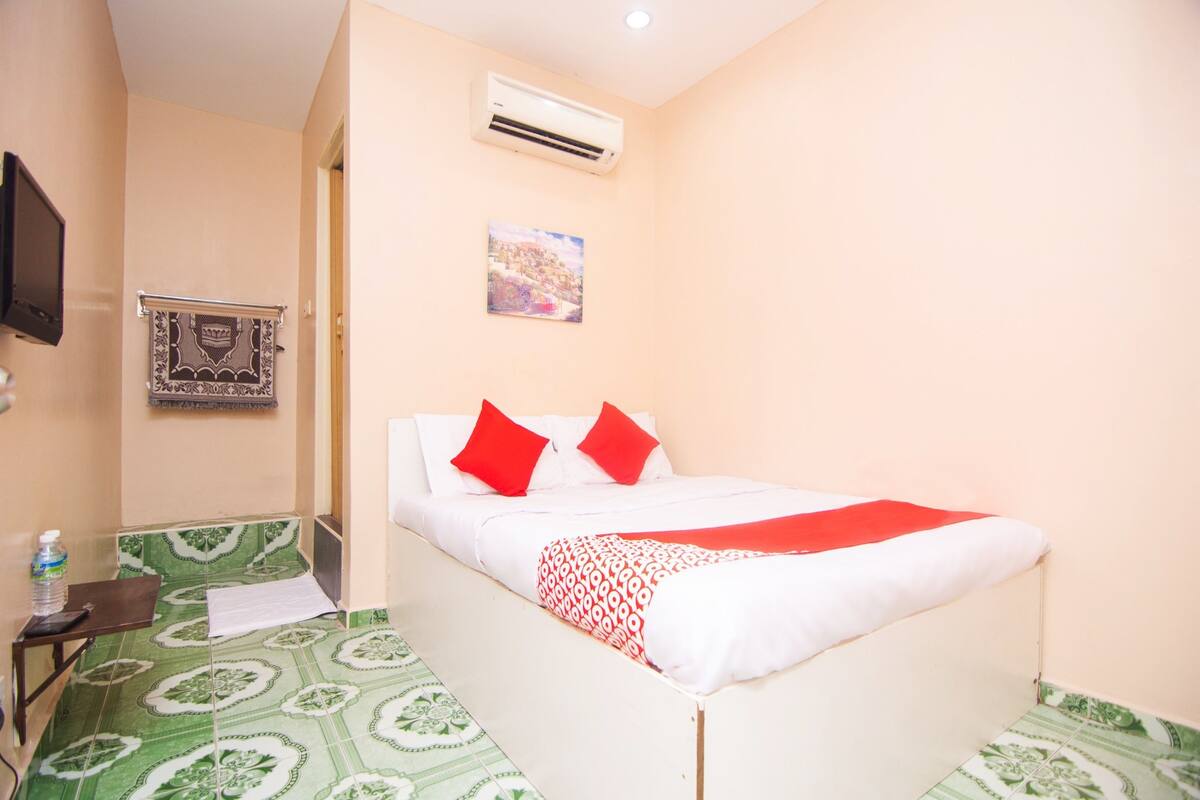 A neatly arranged bedroom with a bed, pillows, a water bottle, and a wall-mounted air conditioner.